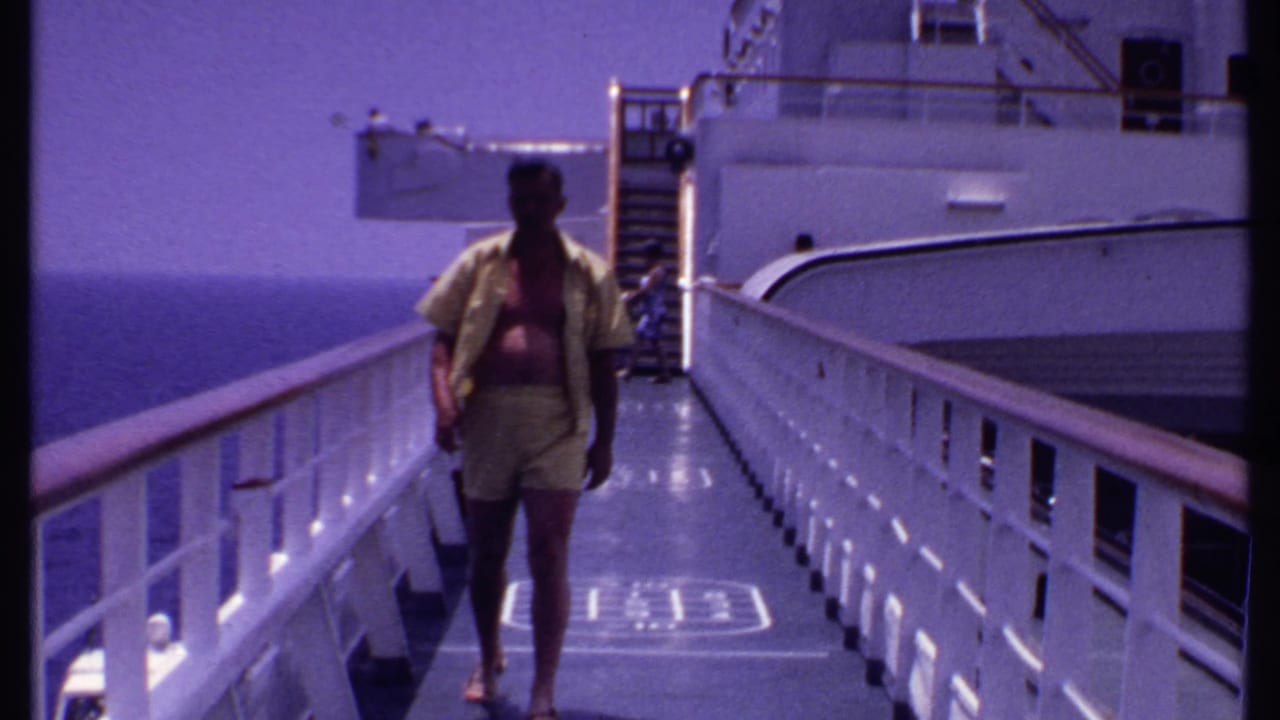 Man walking along a white cruise ship deck with ocean visible on both sides.
