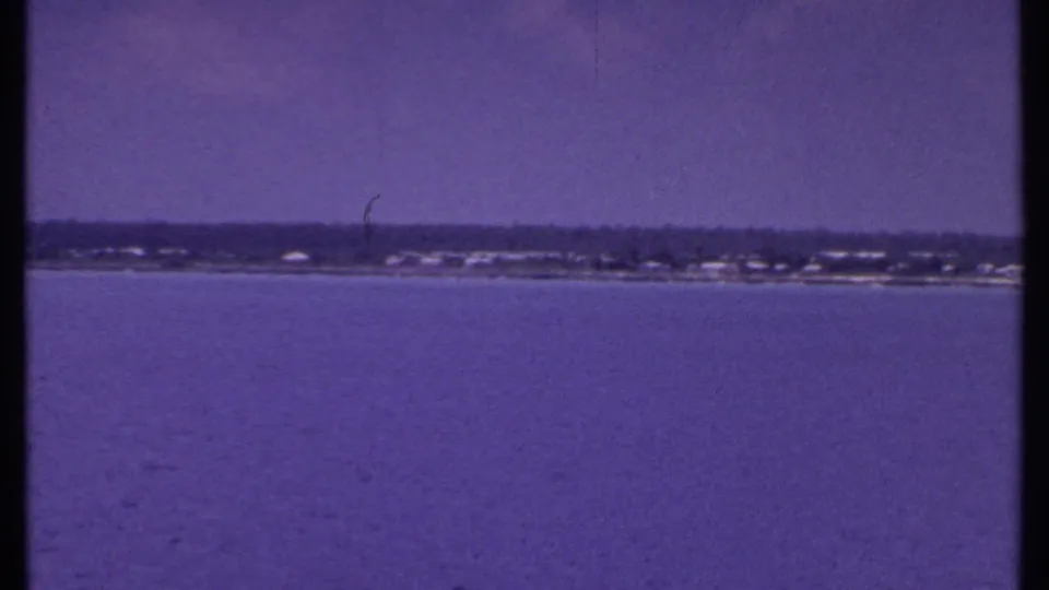 1969 Bahamas 8mm view across calm water toward a distant coast, with visible grain, tint shift, and minor film marks.