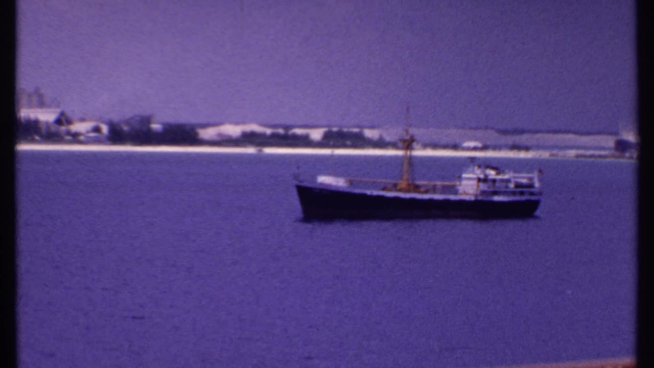 Small dark boat on calm water with distant shoreline and hazy sky.