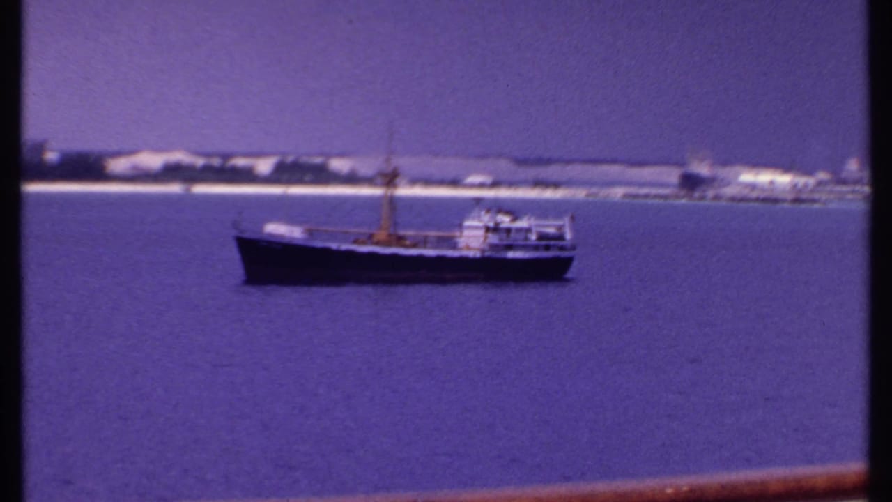 Boat centered on open water with shoreline behind and deck rail at the bottom edge.