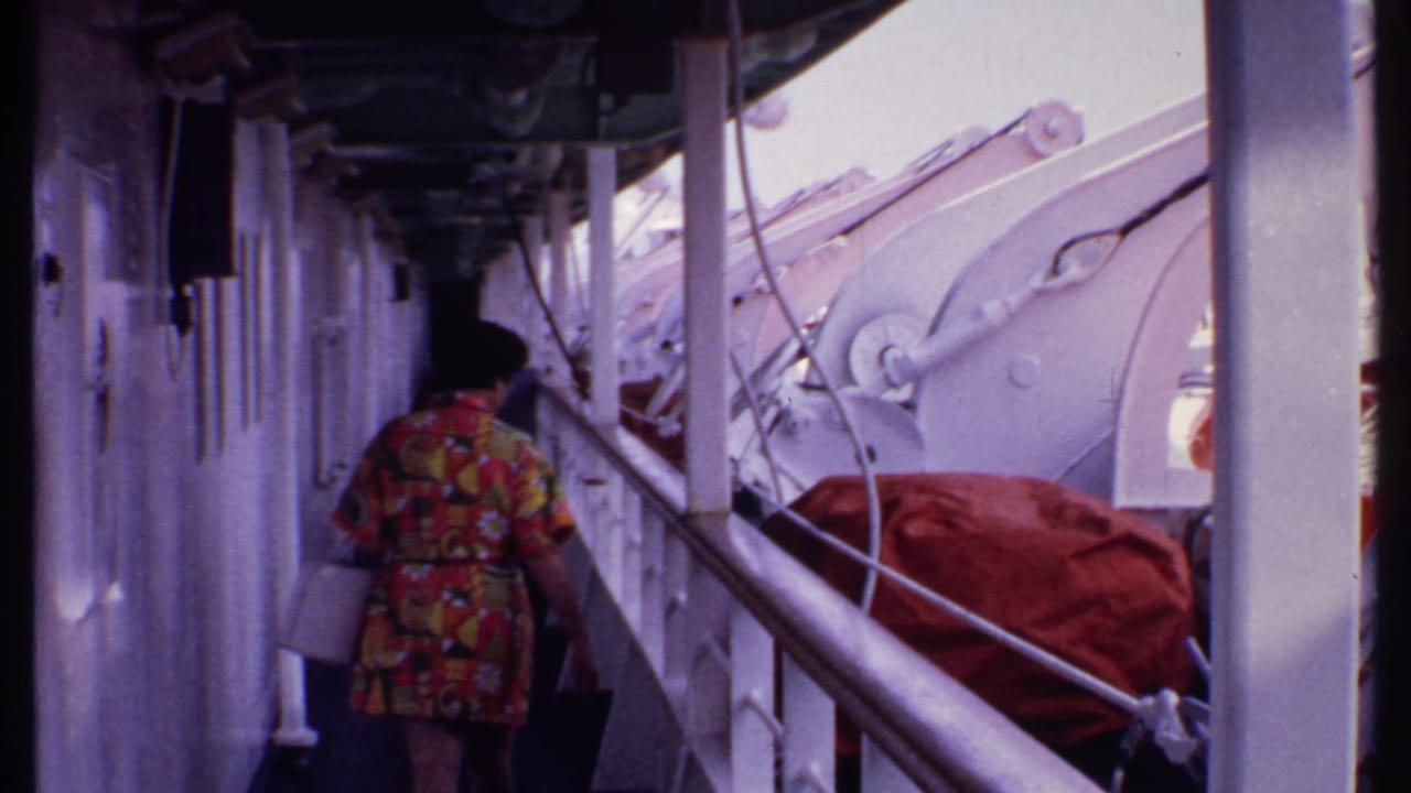 Woman walking farther down a narrow ship deck with railings and lifeboat hardware nearby.