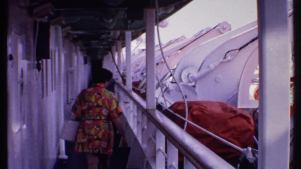 The woman continues down the cruise ship deck, framed by white walls, railings, ropes, and covered boat equipment in the 1969 Bahamas travel clip.