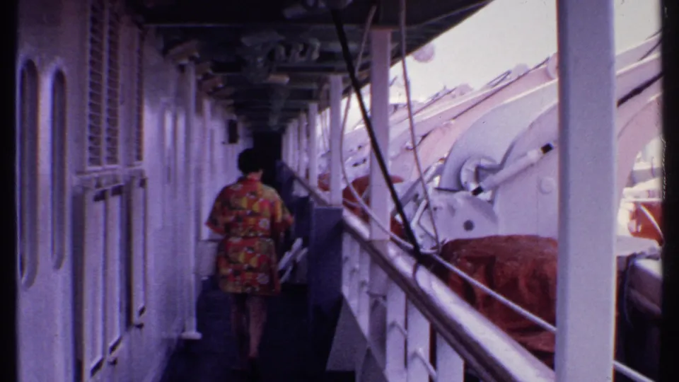 The final frame shows the woman farther down the cruise ship deck, with white wall panels, vertical posts, railings, ropes, and covered equipment around her.