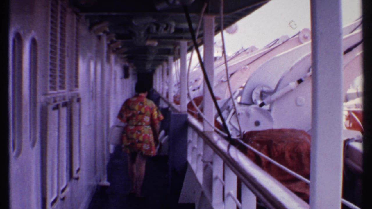 Woman in a floral dress walks away down a narrow ship corridor carrying a white handbag.