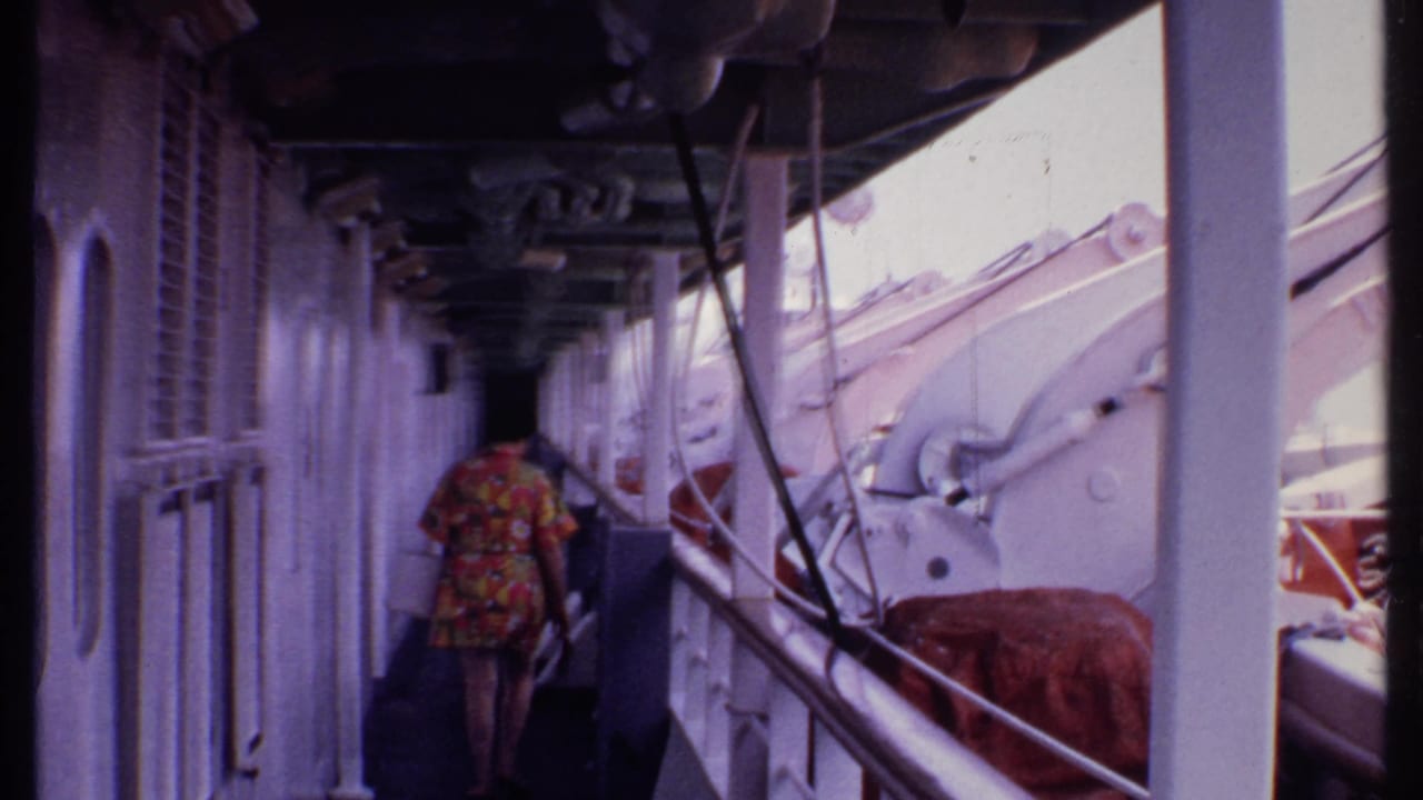 Woman continues down the ship corridor with railings and white structural posts beside her.