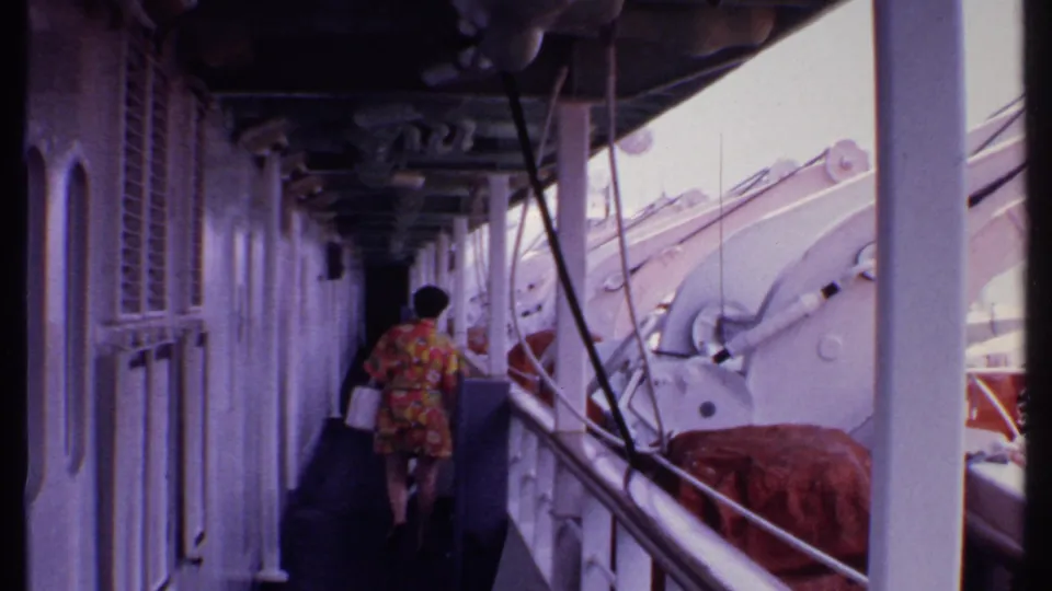 A rear view shows the woman in a bright floral dress walking farther down the ship corridor during the 1969 Bahamas trip.
