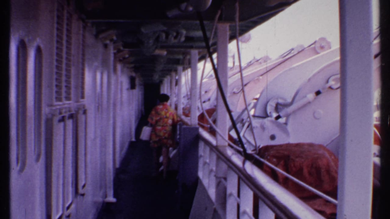 Person in a floral dress walking along a covered ship deck beside lifeboats and railings.