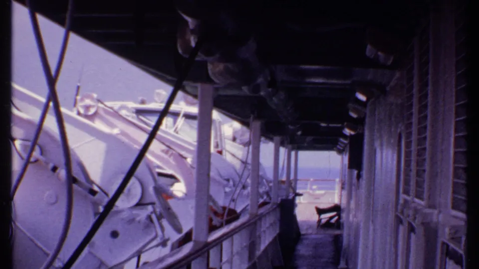 1969 Bahamas ship deck frame showing white lifeboats beside a covered walkway with railings, windows, and ocean at the far end.