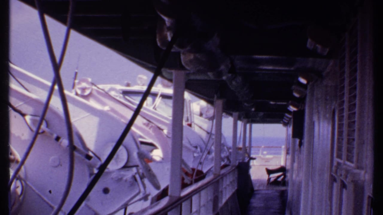 Boat-side view past railings and white equipment toward blue water and sky.