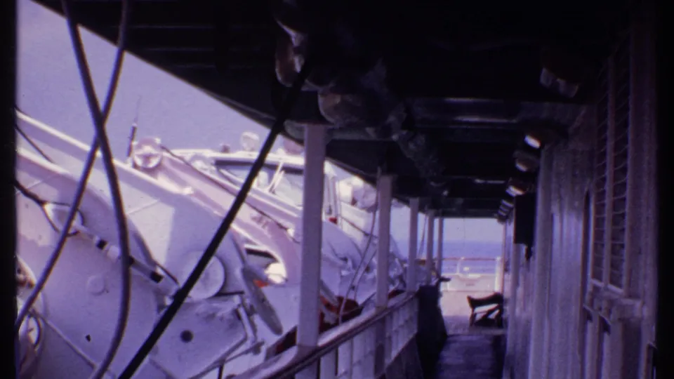 1969 Bahamas 8mm frame looking along a boat-side passage with white hardware, railings, and water beyond.