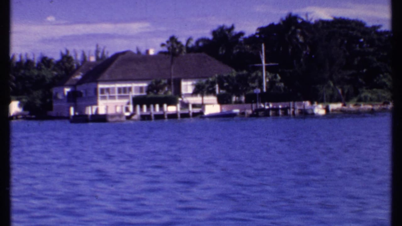 White waterfront house with dock seen across rippled blue water.