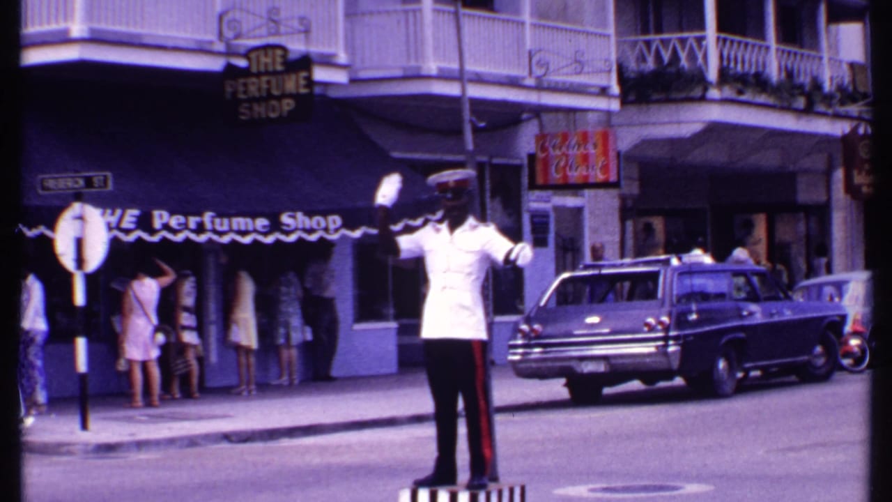 Traffic officer on a striped pedestal outside The Perfume Shop with pedestrians and a station wagon nearby.
