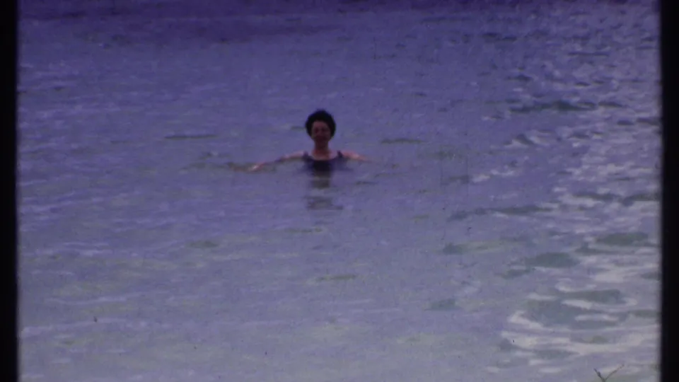 In the Bahamas vacation footage, the woman swims in calm blue ocean water, seen from a handheld home-movie viewpoint.