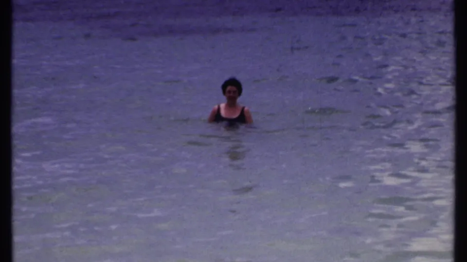 The same Bahamas home-movie sequence shows a woman in dark swimwear floating in shallow-looking blue water.