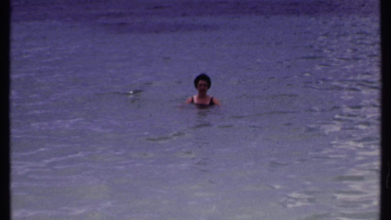 Woman in a dark bathing suit bobbing in calm ocean water.