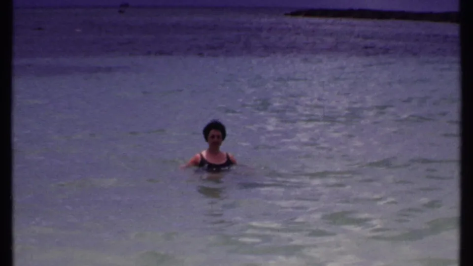 Woman faces the camera while swimming in clear Bahamas water in a 1969 vacation home-movie frame.