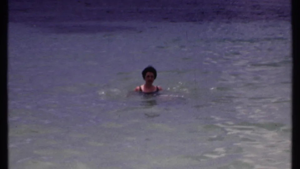 A woman floats or swims slowly in blue-green Bahamas sea water, filmed on 8mm during a 1969 vacation.