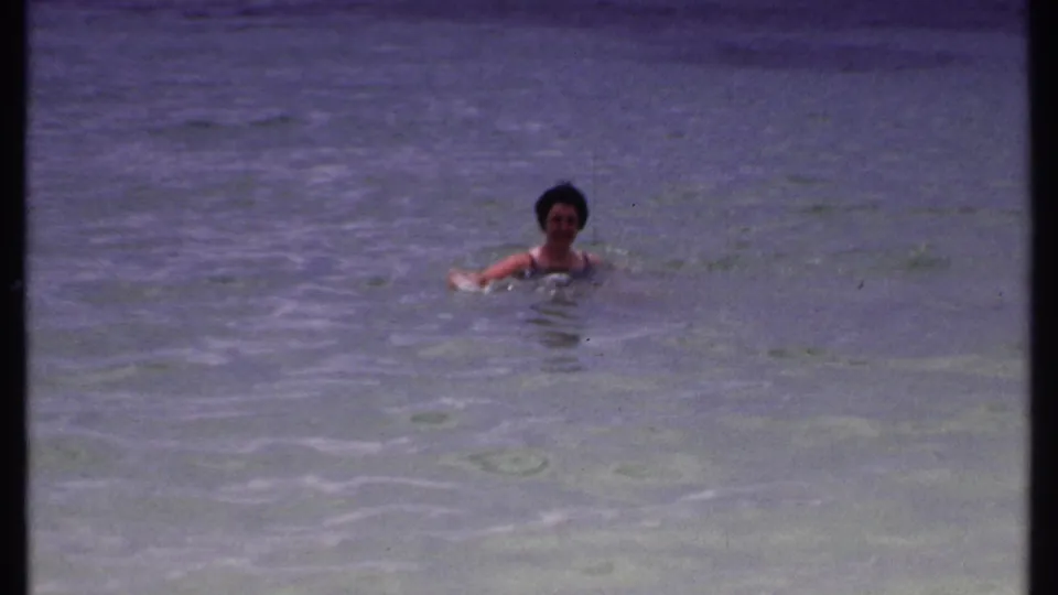 Adult woman appears to float or swim sideways in shallow Bahamas water, seen in soft 8mm color.