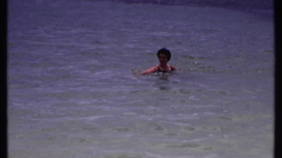 Adult woman in a dark swimsuit swims in calm Bahamas water in 1969 home-movie footage.