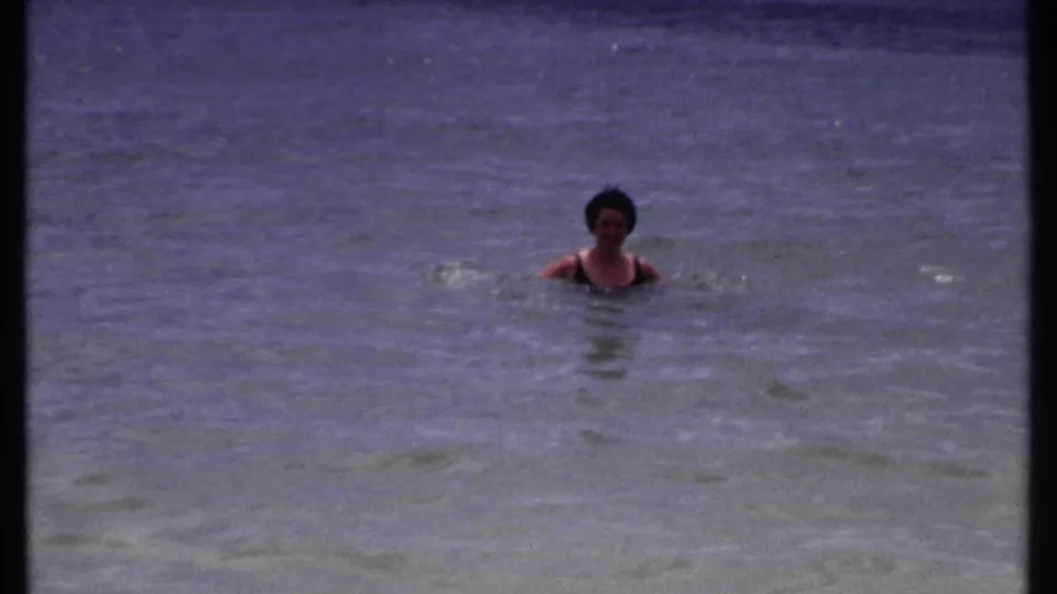 A woman in a dark swimsuit moves through shallow tropical water in color-shifted 1969 8mm footage.