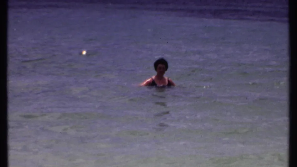 The woman is centered in calm Bahamas water, with visible 8mm grain and a purple-blue vintage color cast.