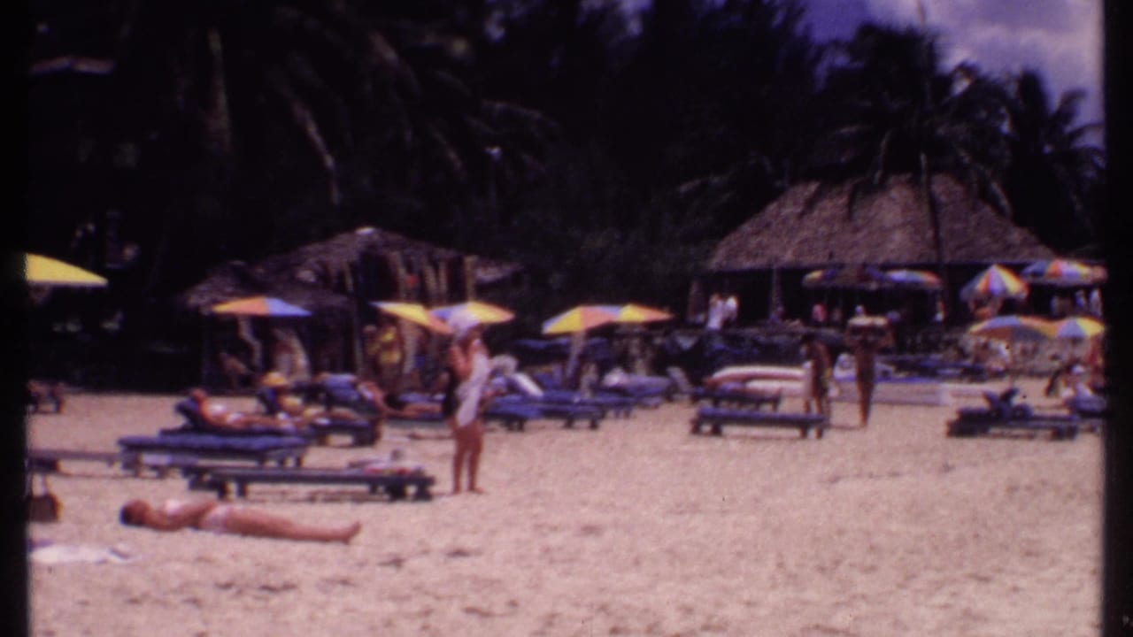 Beach resort guests relax on lounge chairs under striped umbrellas near thatched cabanas.