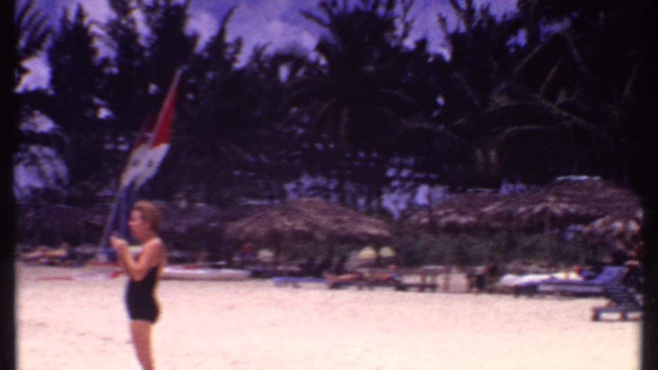 Woman in a black swimsuit holding a red, white, and blue flag on a sandy beach.
