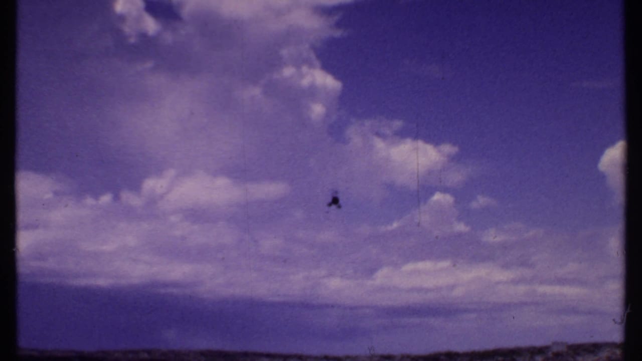 Small helicopter in a clouded sky over a distant waterfront horizon.