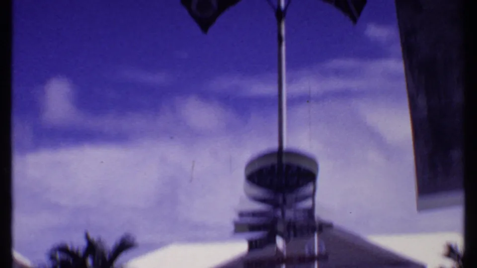 End frame from the 1969 Bahamas home movie with a blurred tilt toward sky, a pole, palm trunk, and building edge.