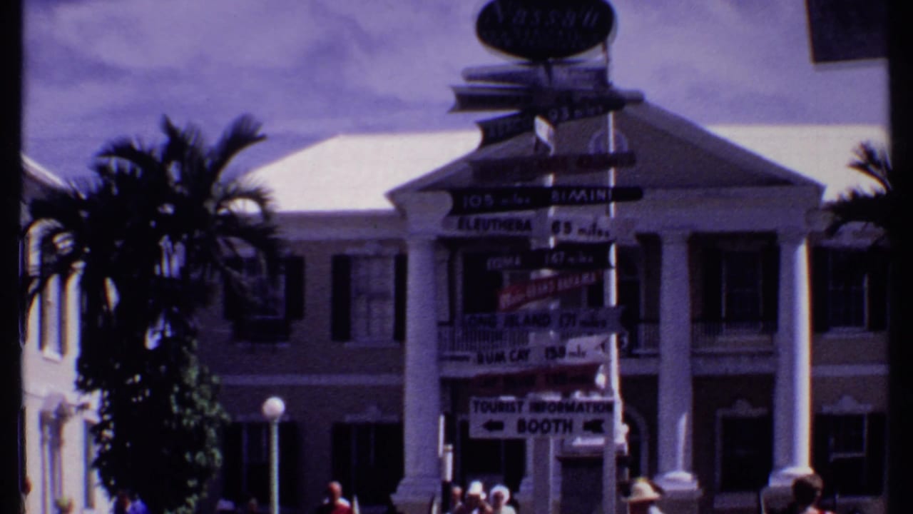 Tourist signpost in front of a columned building with palm trees.