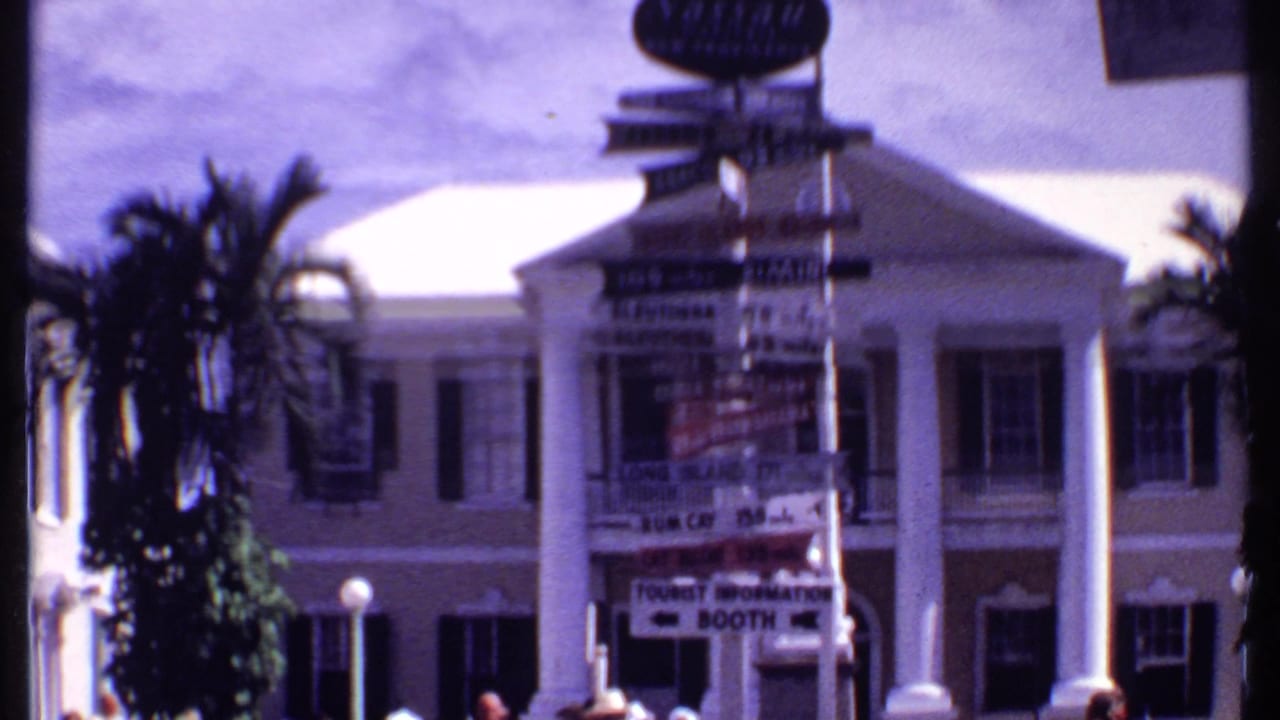 Directional signpost and palm trees outside a white-columned building.