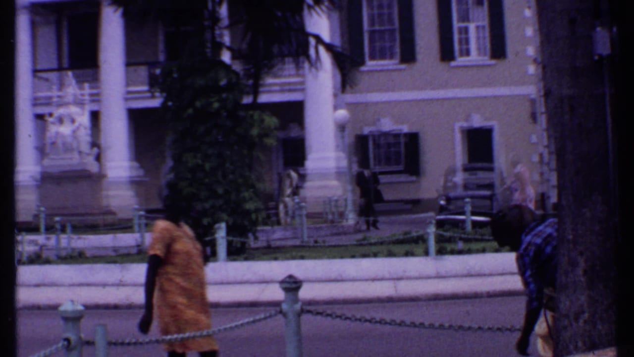 Person walking past chain posts in front of a columned building and statue.