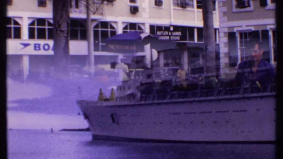 Large cruise ship at a Bahamas port, seen through handheld 8mm framing with nearby street signs and cars in the background.