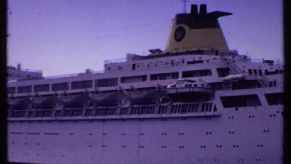 1969 Bahamas 8mm frame showing the upper side of a white cruise ship with lifeboats, portholes, decks, and a marked funnel.