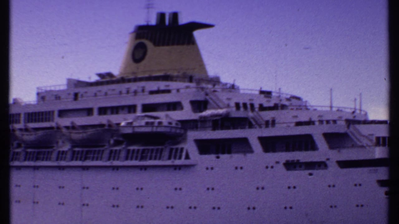 Cruise ship upper decks, lifeboats, funnel, and rows of portholes under dusk sky.