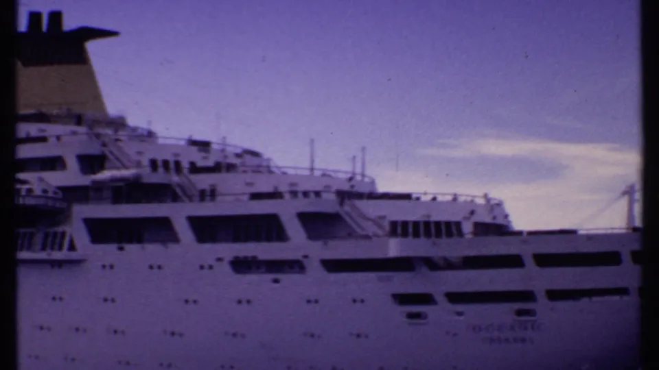 1969 Bahamas 8mm frame showing the ship's side from a closer pan position, with portholes, dark windows, and faint hull lettering.