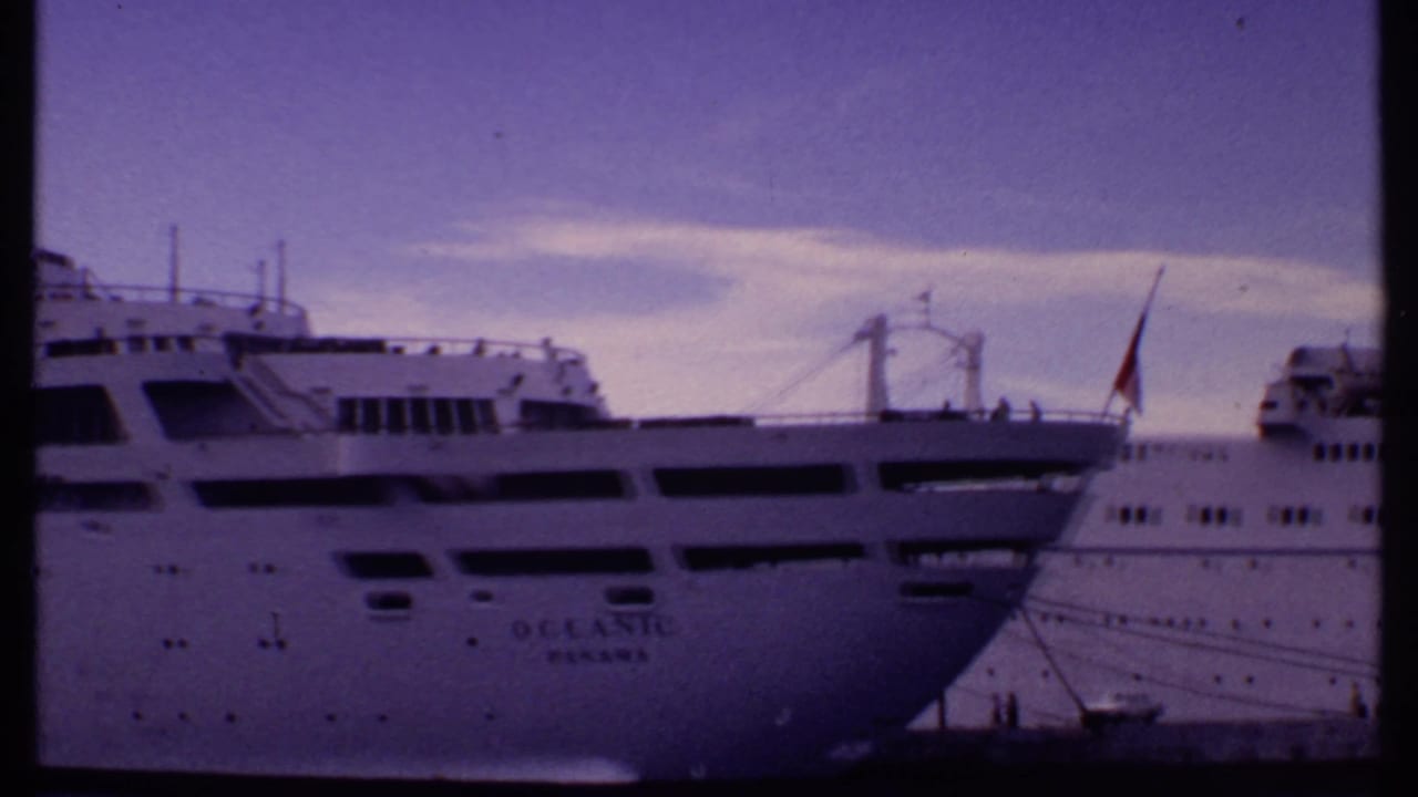 1969 Bahamas 8mm frame showing a large white cruise ship docked at the waterfront with harbor buildings partly visible.