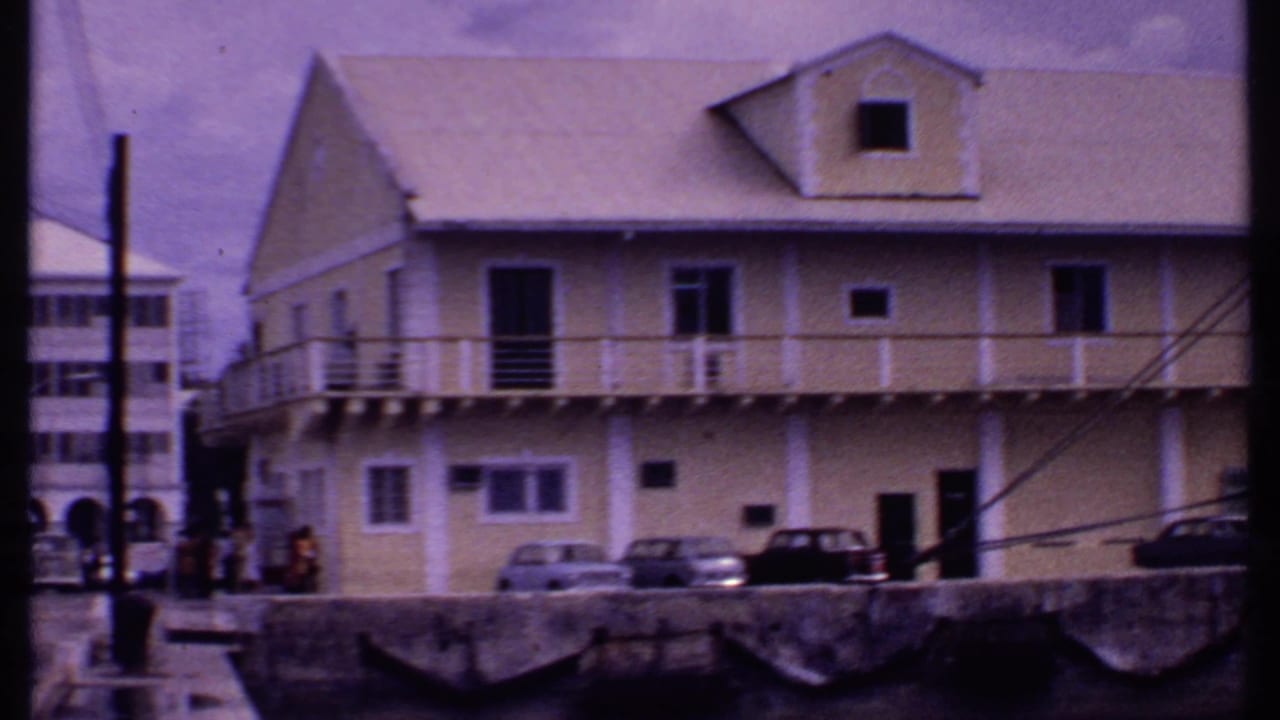 Waterfront building with balcony, parked cars, and part of a cruise ship nearby.