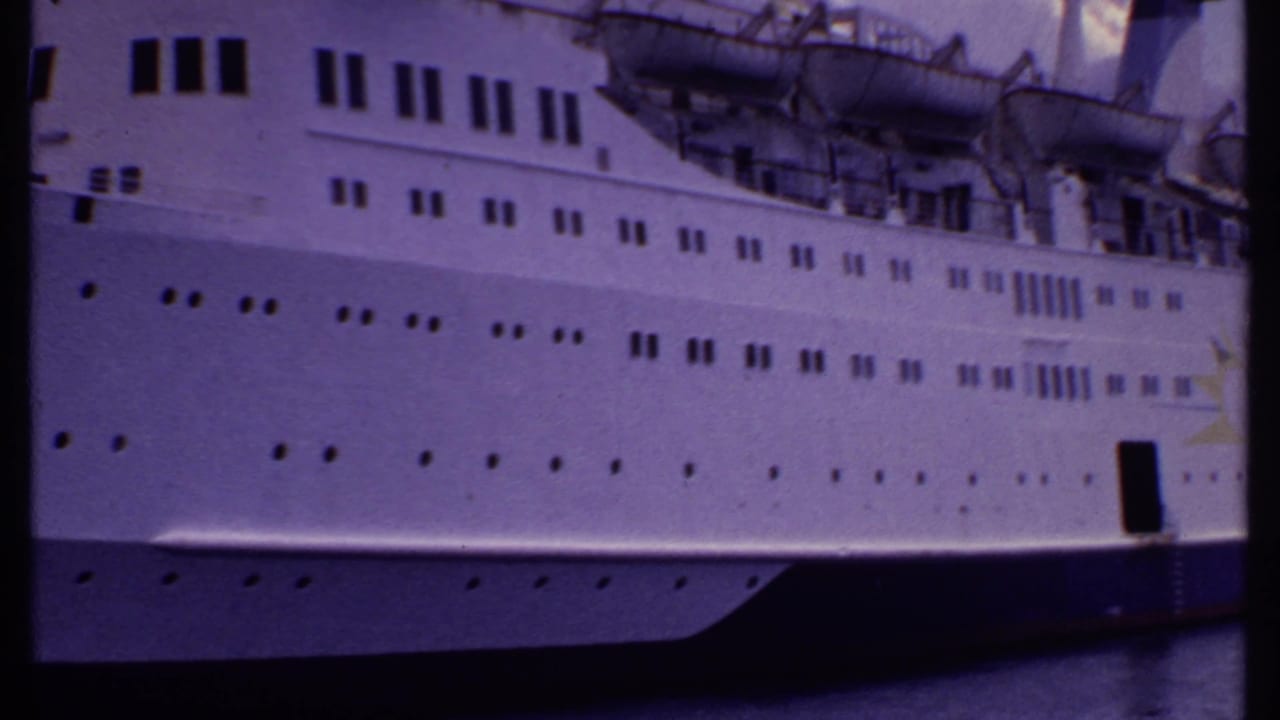 1969 Bahamas 8mm frame showing the side of a large white cruise ship with rows of portholes and lifeboats above the hull.