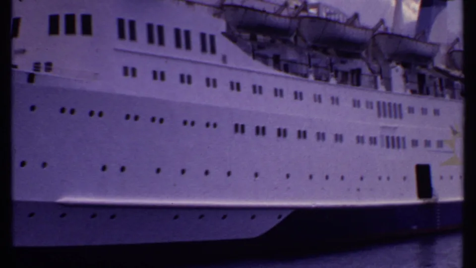 1969 Bahamas 8mm frame showing the side of a large white cruise ship with rows of portholes and lifeboats above the hull.