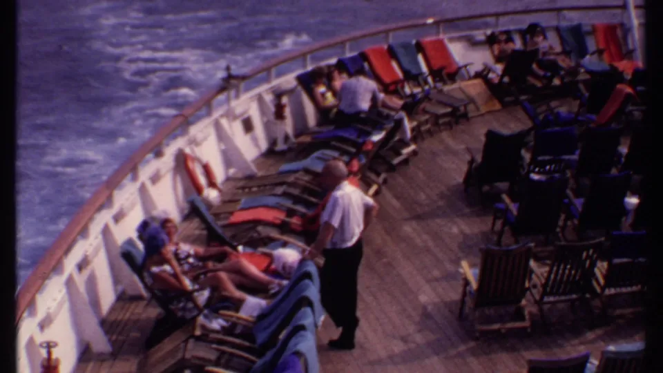1969 Bahamas cruise deck view with passengers reclining in colorful lounge chairs while a uniformed crew member stands nearby.