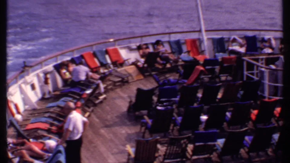 1969 Bahamas cruise footage frame showing passengers spread across deck chairs on an open ship deck with railings and sea wake visible.