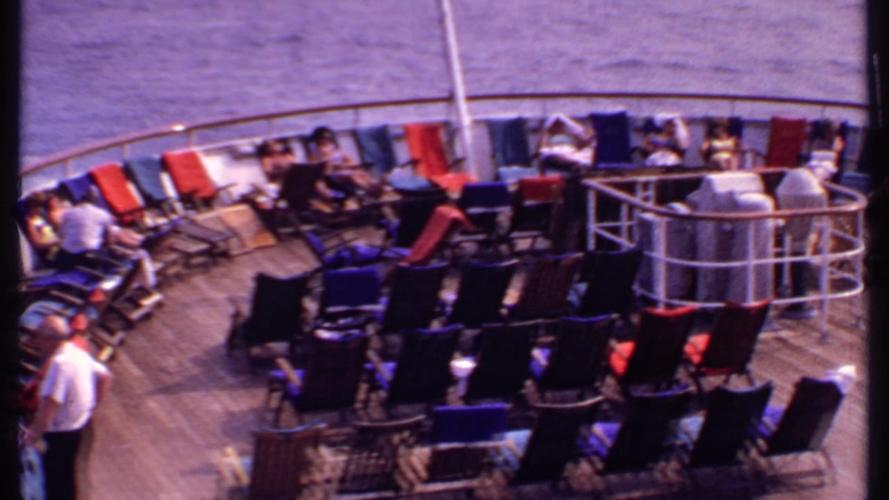 1969 Bahamas cruise ship deck with rows of red, blue, and dark lounge chairs and passengers near the railing.