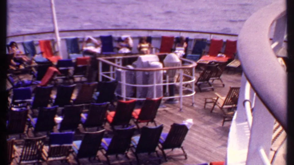 1969 Bahamas cruise deck view showing passengers seated near railings and many lounge chairs arranged across the wooden deck.