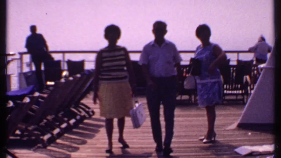 1969 Bahamas cruise ship deck with three adult passengers standing near lounge chairs against a bright ocean backdrop.