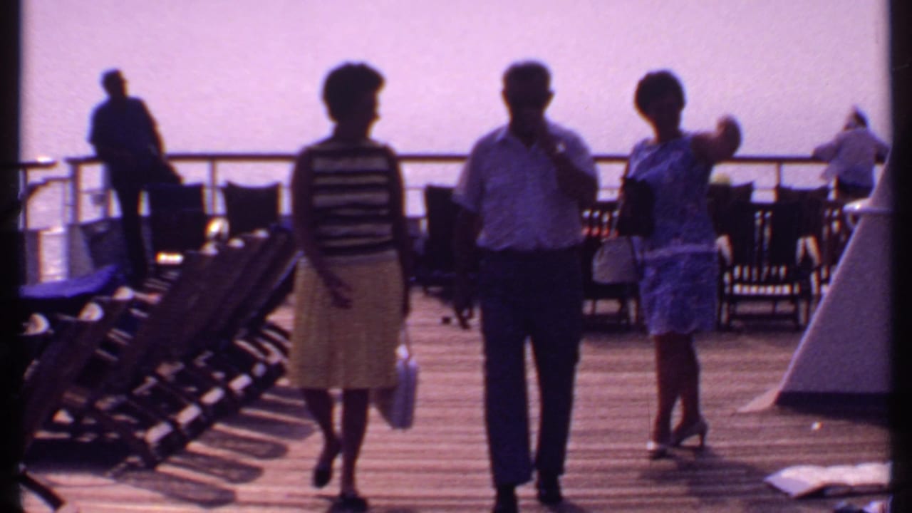 In 1969 Bahamas cruise footage, three adults approach the camera on a deck lined with lounge chairs, with ocean visible beyond the rail.