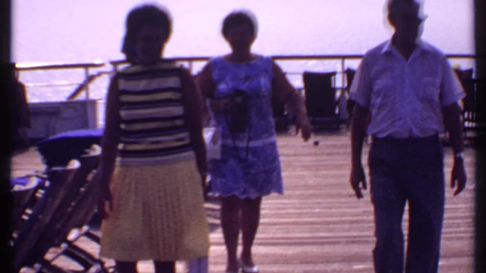 Near the end of the clip, the adults pass close to the camera on the Bahamas cruise deck, with deck chairs, railings, and ocean still visible.
