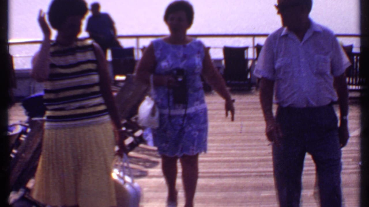 1969 Bahamas cruise footage shows passengers in summer clothing walking across a sunlit ship deck with railings and chairs nearby.