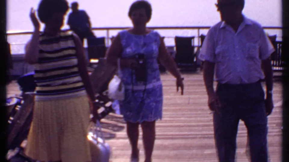 1969 Bahamas cruise footage shows passengers in summer clothing walking across a sunlit ship deck with railings and chairs nearby.