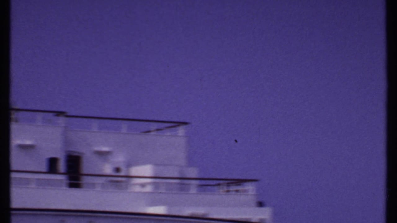 Bahamas 1969 home-movie frame showing white cruise ship decks, railings, and upper structure beneath a saturated blue-purple sky.